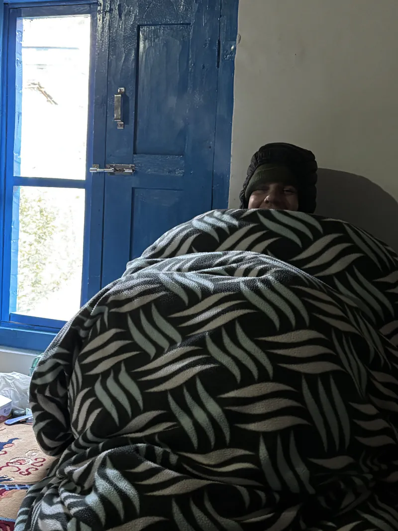 Leo wrapped up to the eyes in a thick patterned blanket next to a blue window