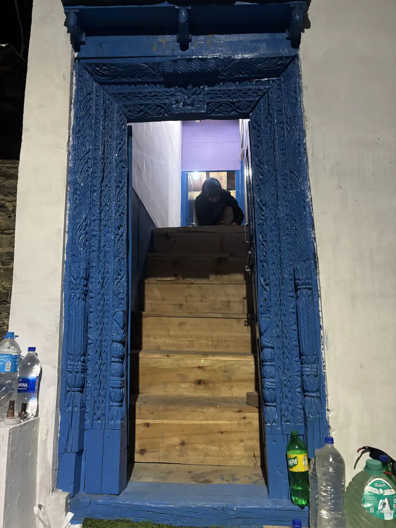 The carved blue door at night, with wooden stairs behind it