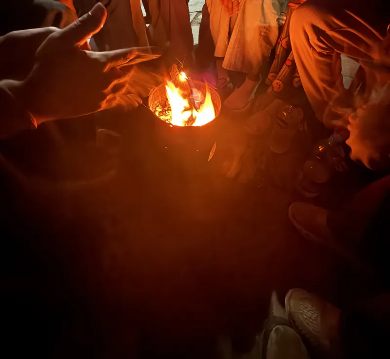 Hands held out over a small fire in a metal bucket at night