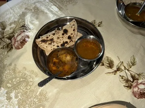 A steel plate with homemade rotis, a bowl of eggs in gravy and a bowl of dal on a flowered tablecloth