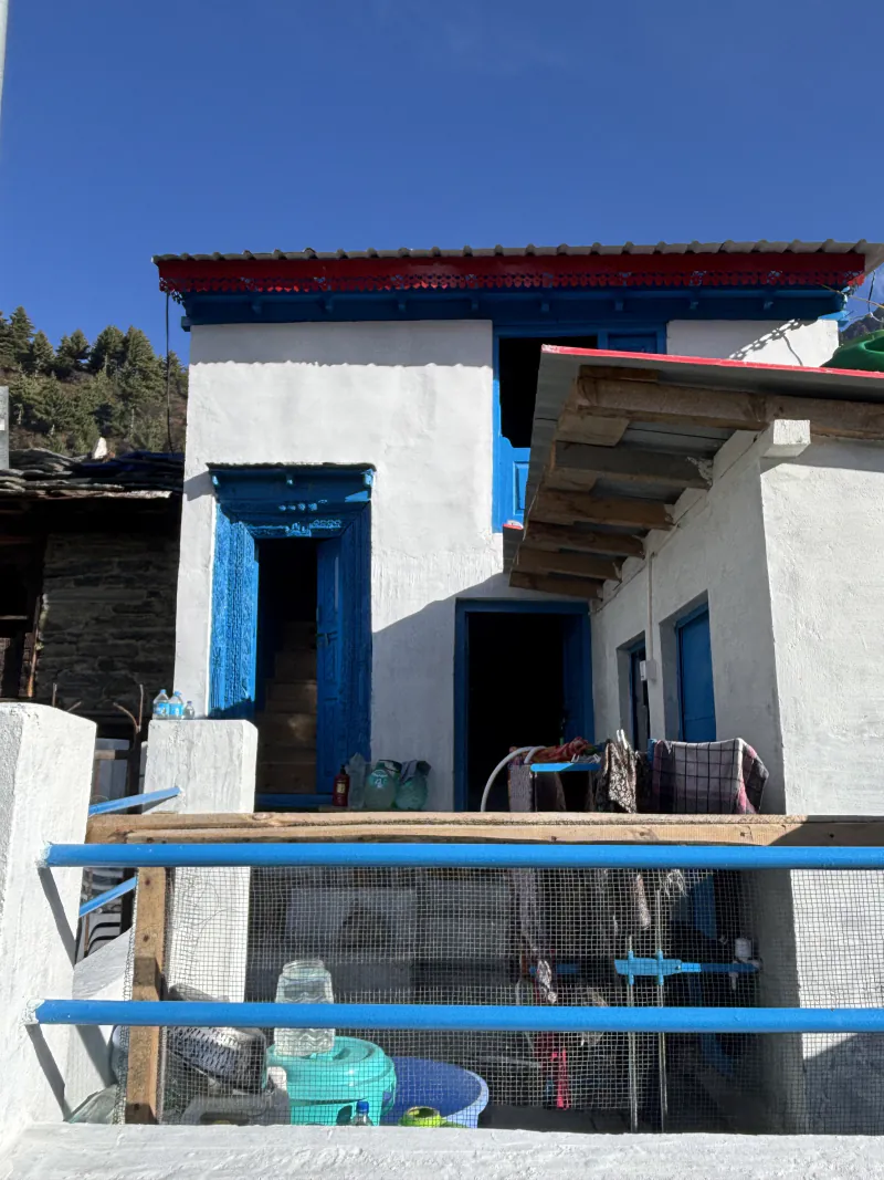 Mati's house in the sun: white walls, a carved blue door and a red band under the roof