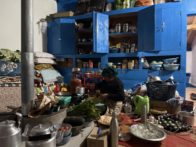 Mati cooking on the floor of her blue kitchen, with fresh greens, kettles and pots around her