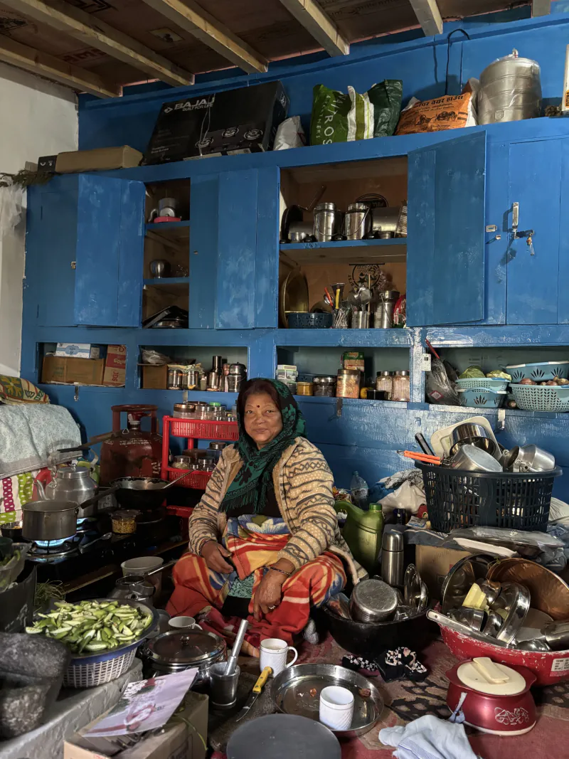 Mati sitting in her kitchen in front of blue-painted shelves full of steel pots and tins