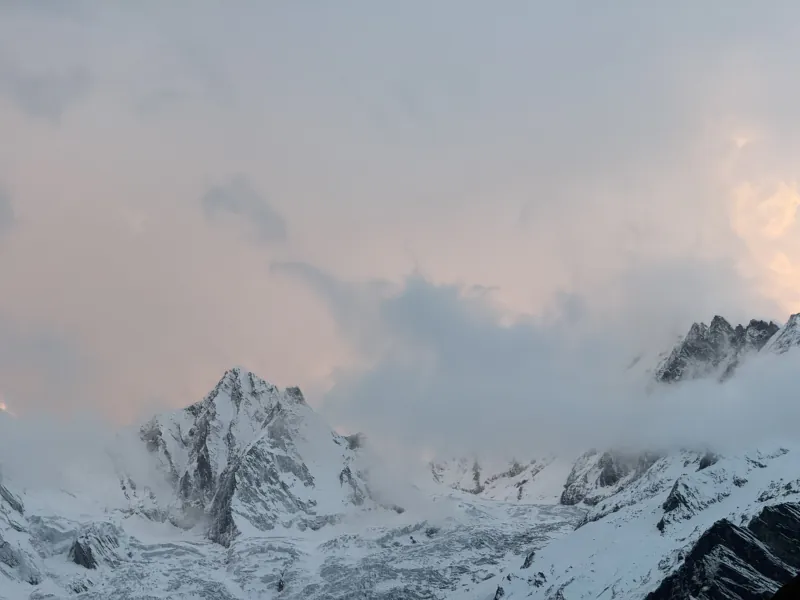 Snow peaks disappearing into clouds in pink evening light