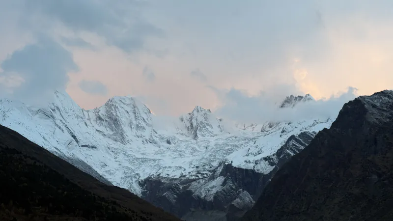 Snow peaks and glacier at dusk under a pale pink sky