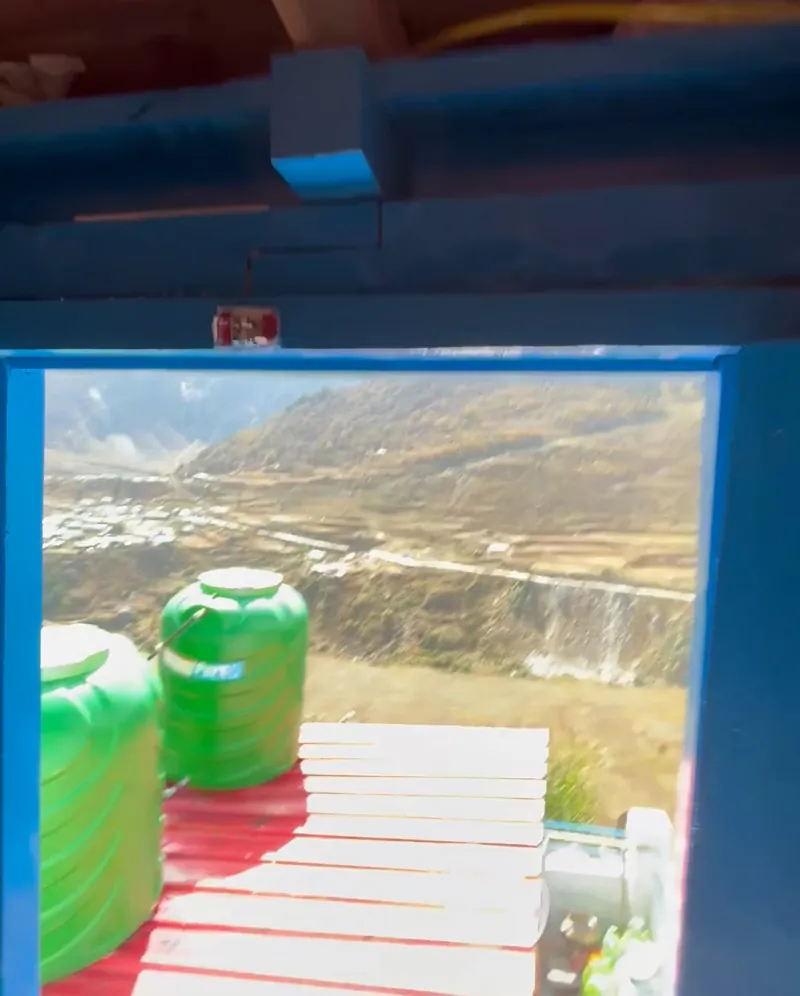 View through a blue door onto the roof: red floor, green water tanks and the valley below