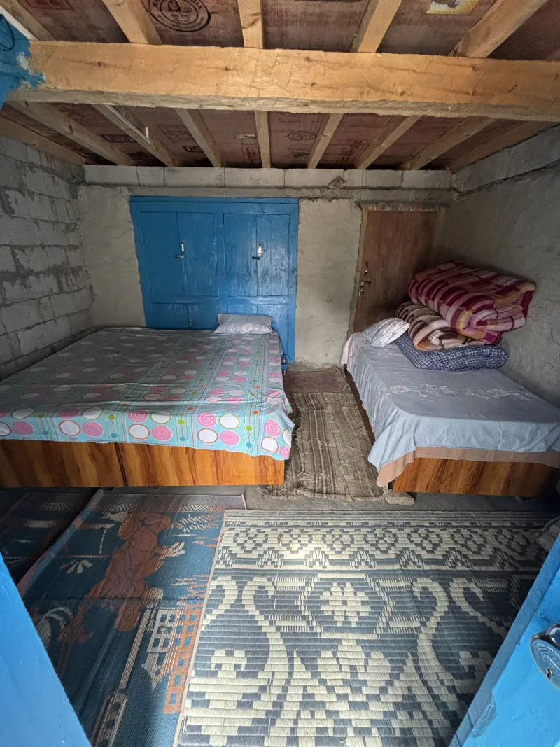 Guest room with two beds, folded blankets, a blue cupboard and woven mats on the floor