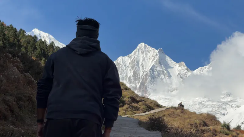 Sumit walking up a trail towards a snow peak under a deep blue sky
