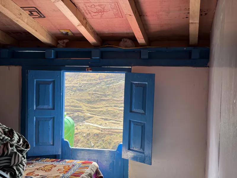 Upstairs guest room with blue wooden shutters open onto the terraced fields of the valley